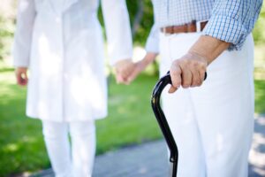Close-up of disabled female hand holding cane with her doctor walking near by